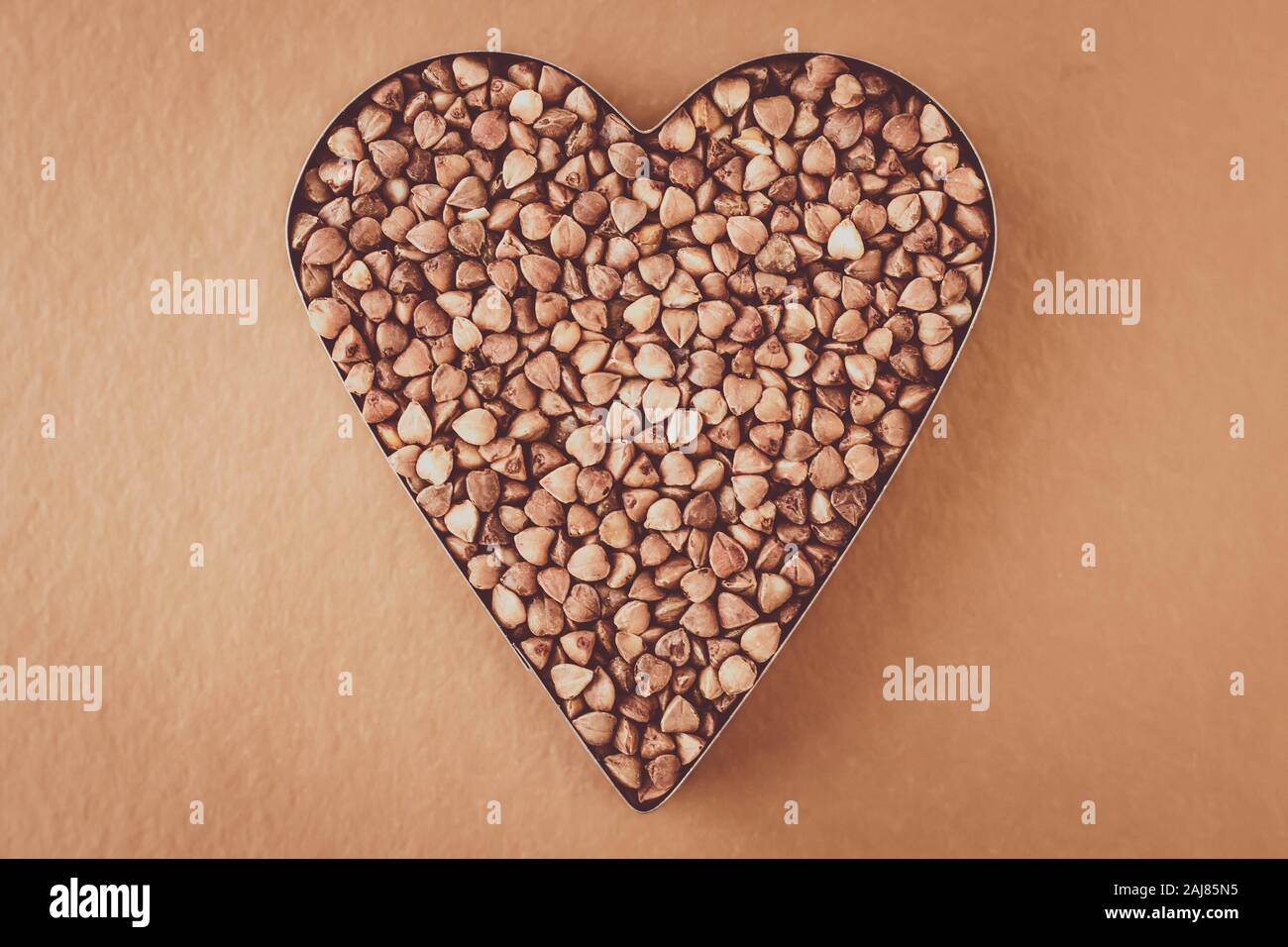 Cumulo di chicchi di grano saraceno su sfondo marrone. A forma di cuore. Grappolo di semi. Dieta carboidrato concept Foto Stock