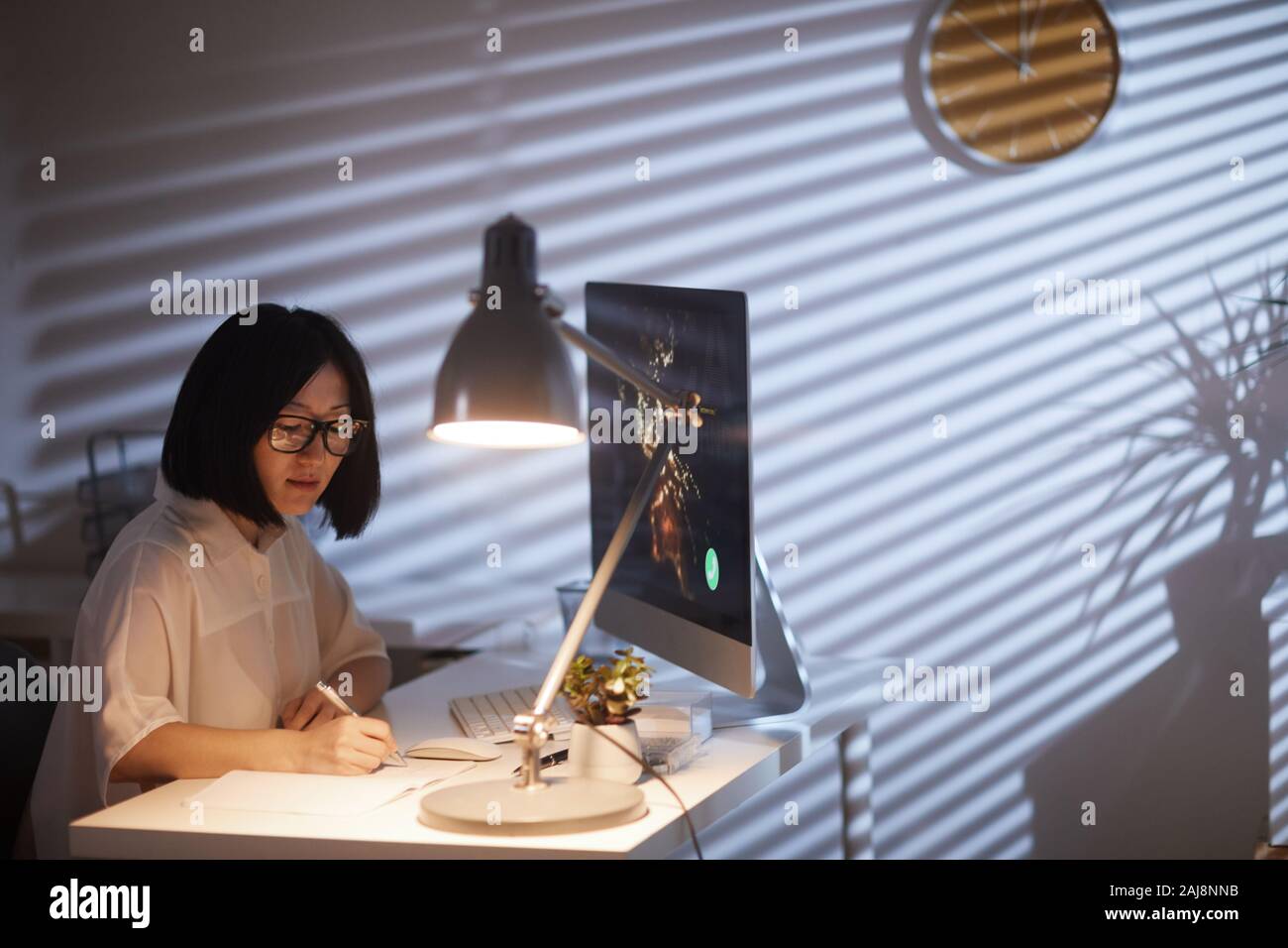 Asian imprenditrice seduti alla scrivania davanti al monitor del computer e di rendere note la pianificazione ha il suo lavoro e lavorare fino a tardi in ufficio Foto Stock