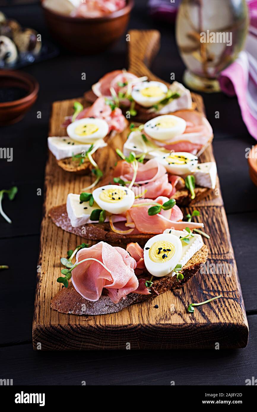 Bruschetta con prosciutto/jamon Italiano tradizionale di antipasto. Delizioso spuntino con pane, formaggio brie e uova di quaglia. Health food, tapas Foto Stock