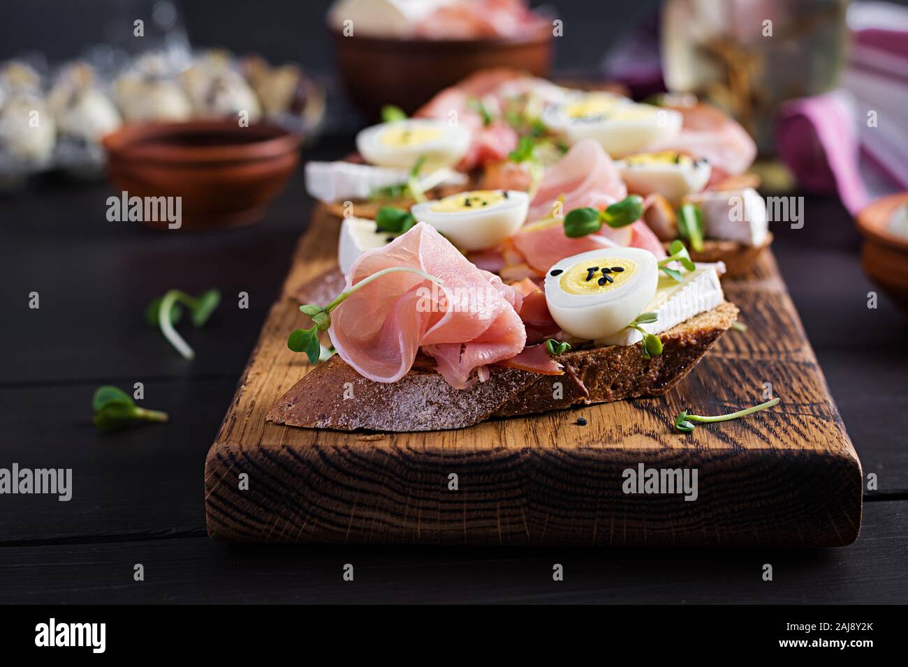 Bruschetta con prosciutto/jamon Italiano tradizionale di antipasto. Delizioso spuntino con pane, formaggio brie e uova di quaglia. Health food, tapas Foto Stock