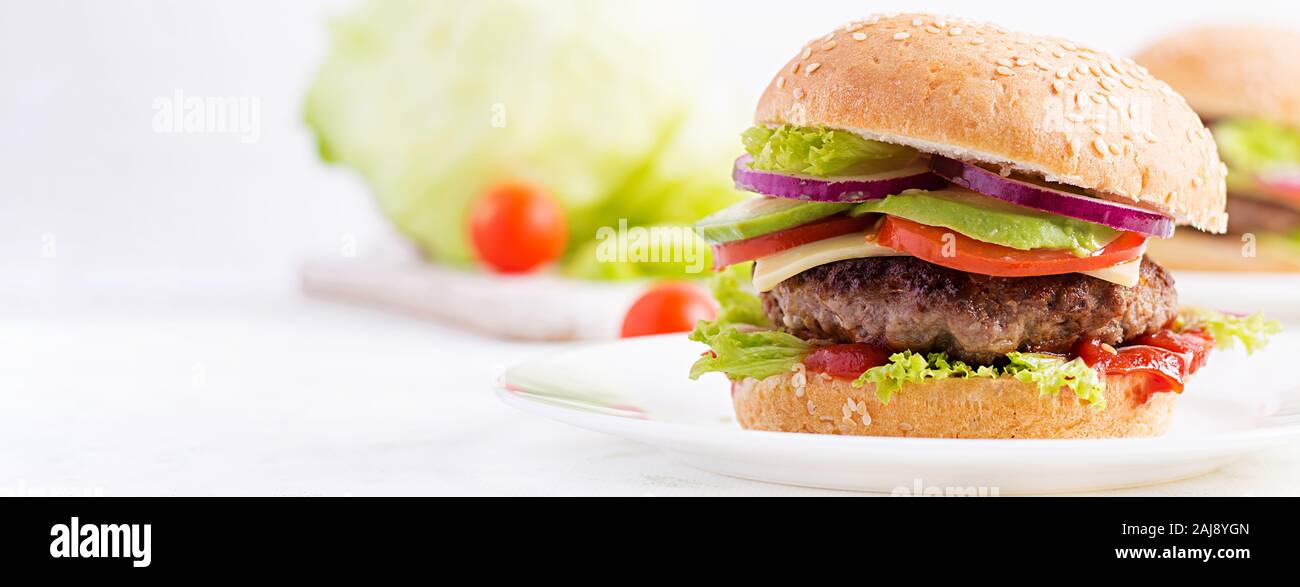 Grande panino - hamburger burger con carne di manzo, avocado, pomodori e cipolle rosse su sfondo chiaro. Cucina americana. Banner. Il Fast Food Foto Stock