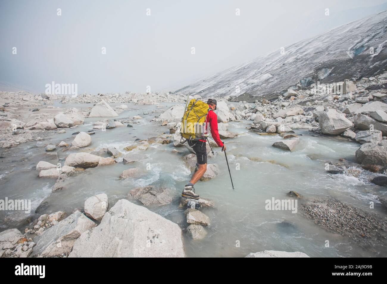 Backpacker utilizza massi di grandi dimensioni per attraversare il fiume accanto al ghiacciaio. Foto Stock