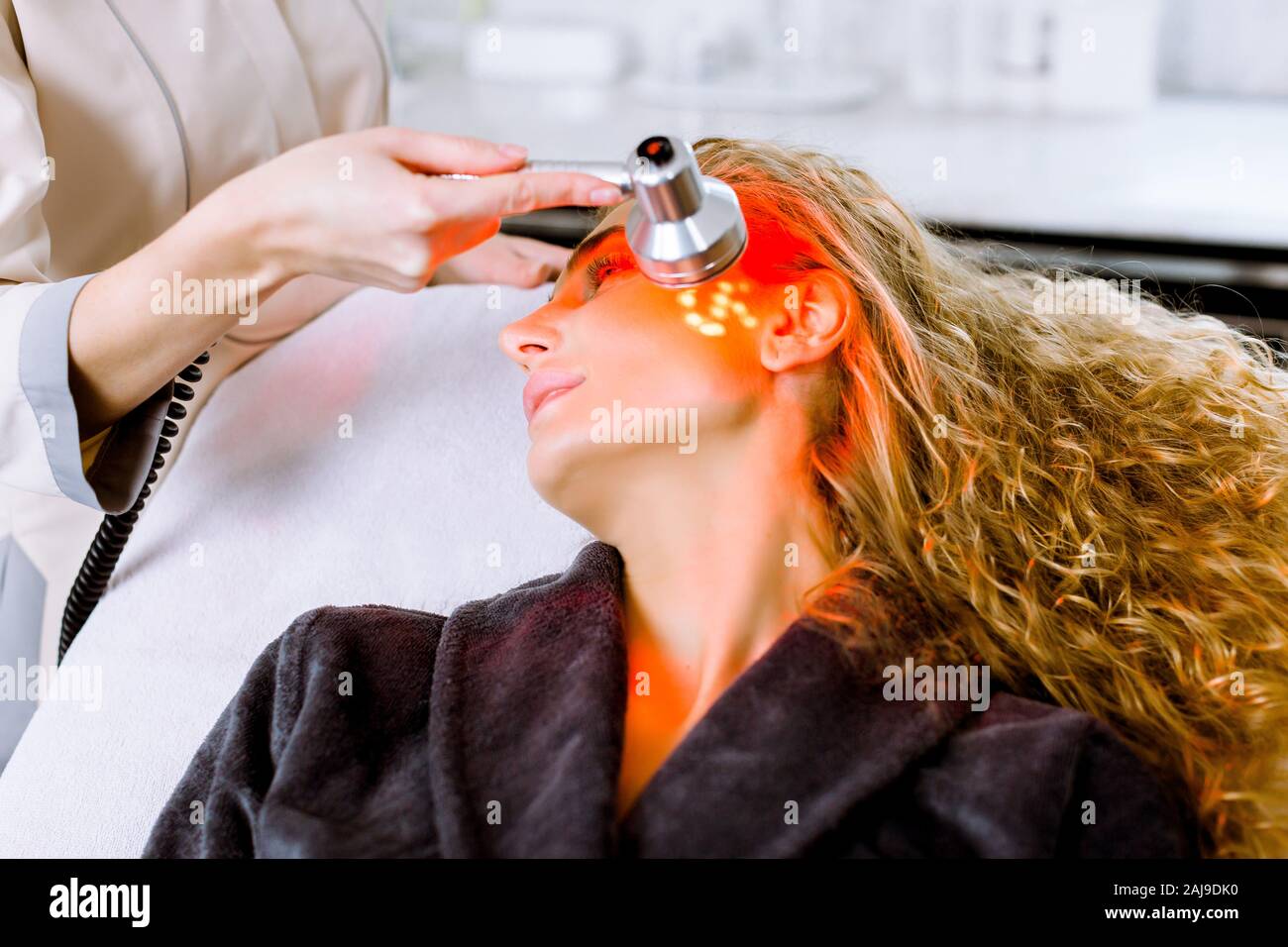 Estetista facendo luce LED rossa terapia per donna bionda in un salone di bellezza, foto del viso per la terapia dei pori della pelle detergente. Anti-trattamenti di invecchiamento e photo r Foto Stock