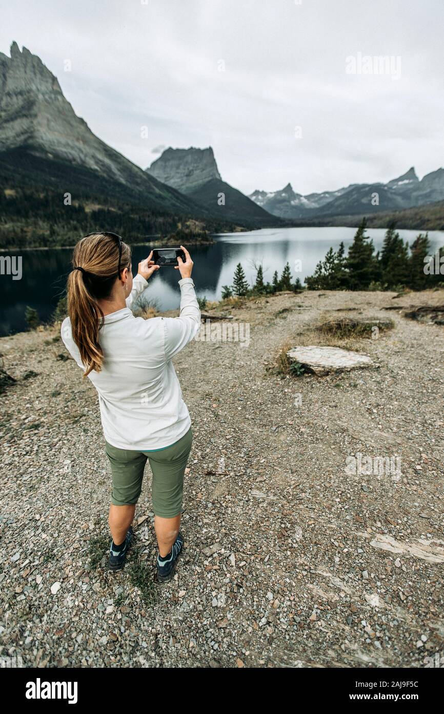 Donna usa il telefono cellulare per scattare foto della vista sulle montagne, Montana Foto Stock