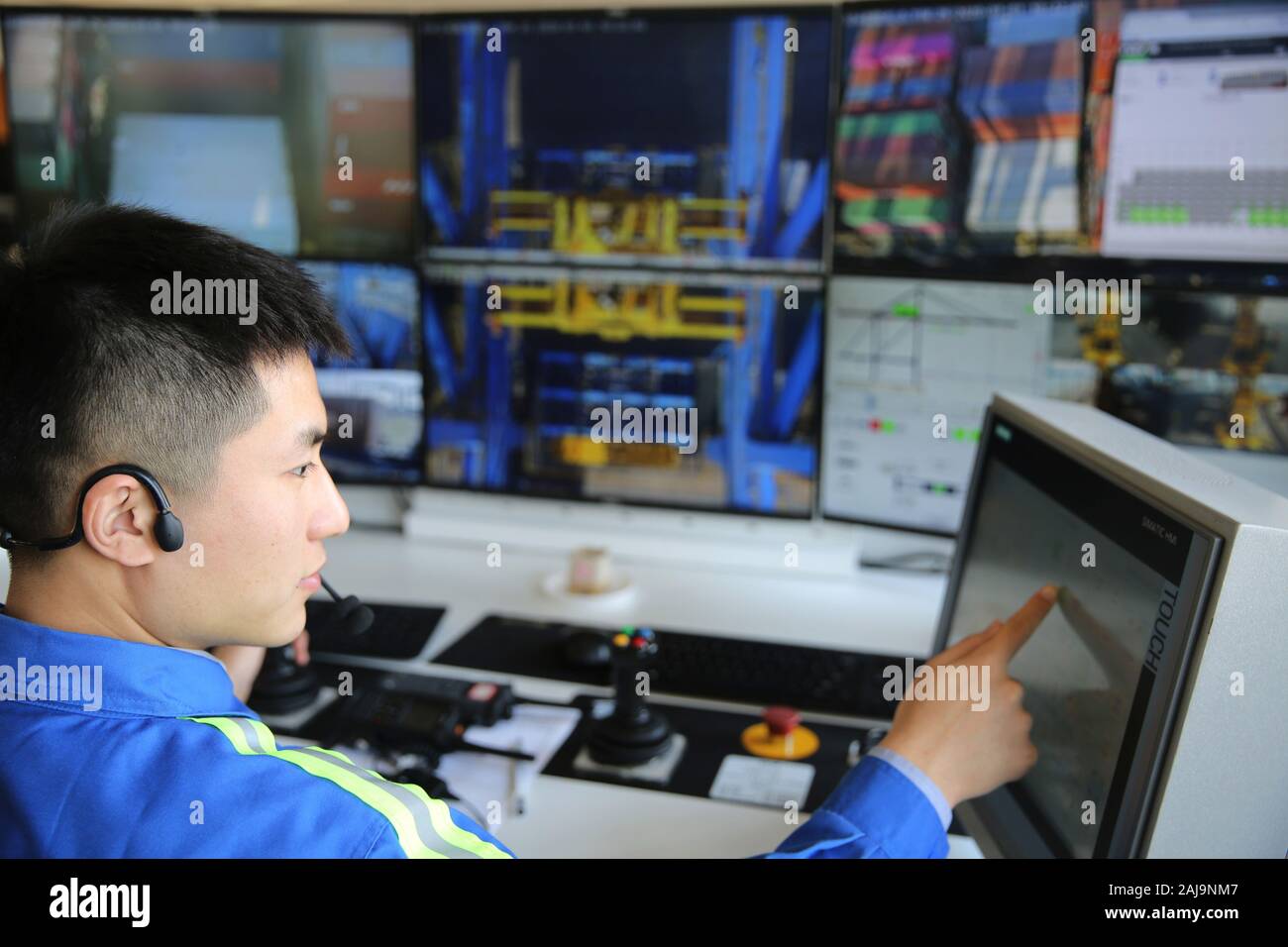 Un lavoratore cinese remote-controlla una gru per il sollevamento di un contenitore da un carrello senza equipaggio e caricarlo su una nave in sala di controllo presso il porto di Qingdao Foto Stock