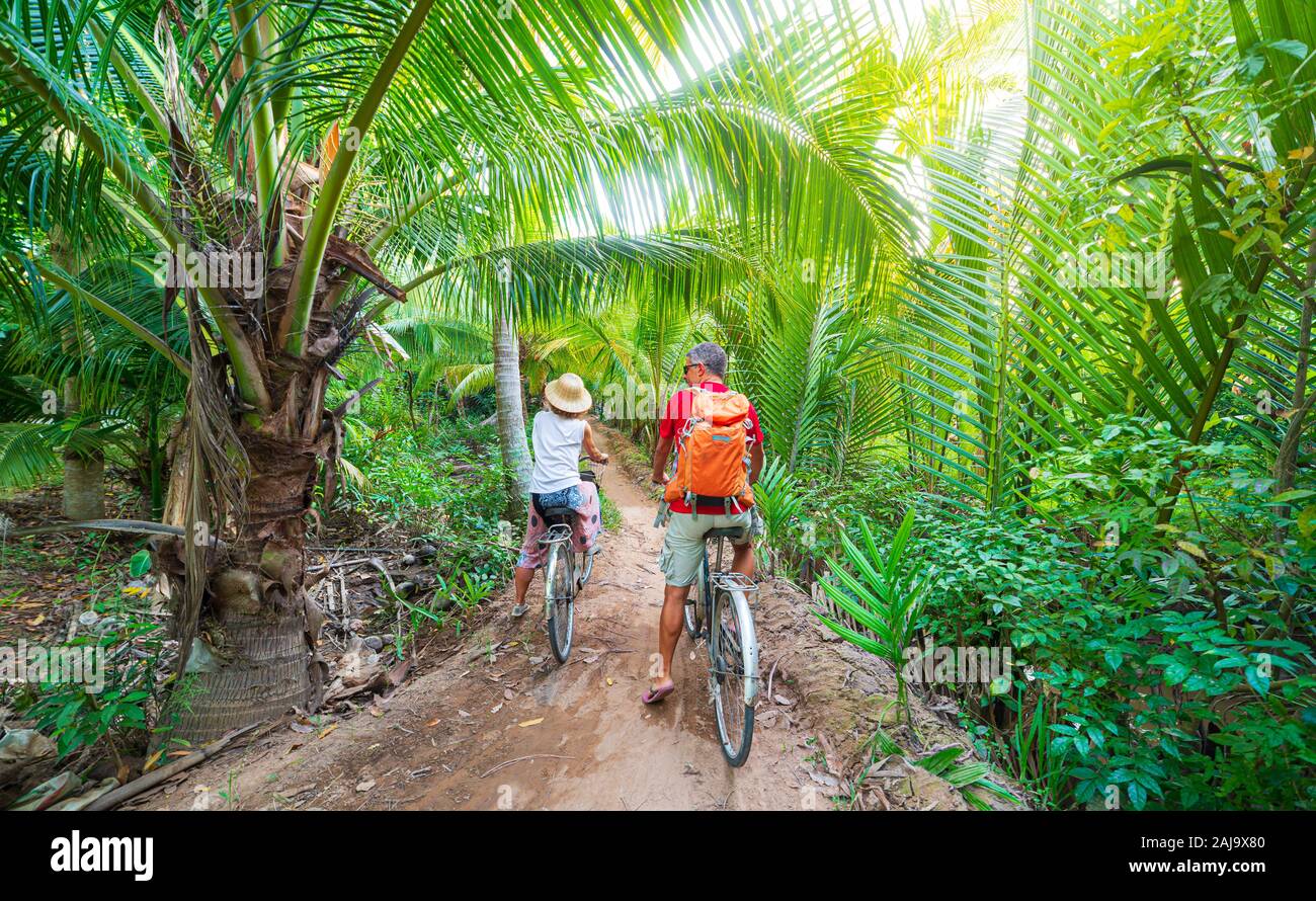 Coppia turistico equitazione bicicletta nella regione del Delta del Mekong, Ben tre, Vietnam del Sud. Donna e uomo avendo divertimento escursioni in bicicletta sul sentiero tra il verde woodl tropicale Foto Stock