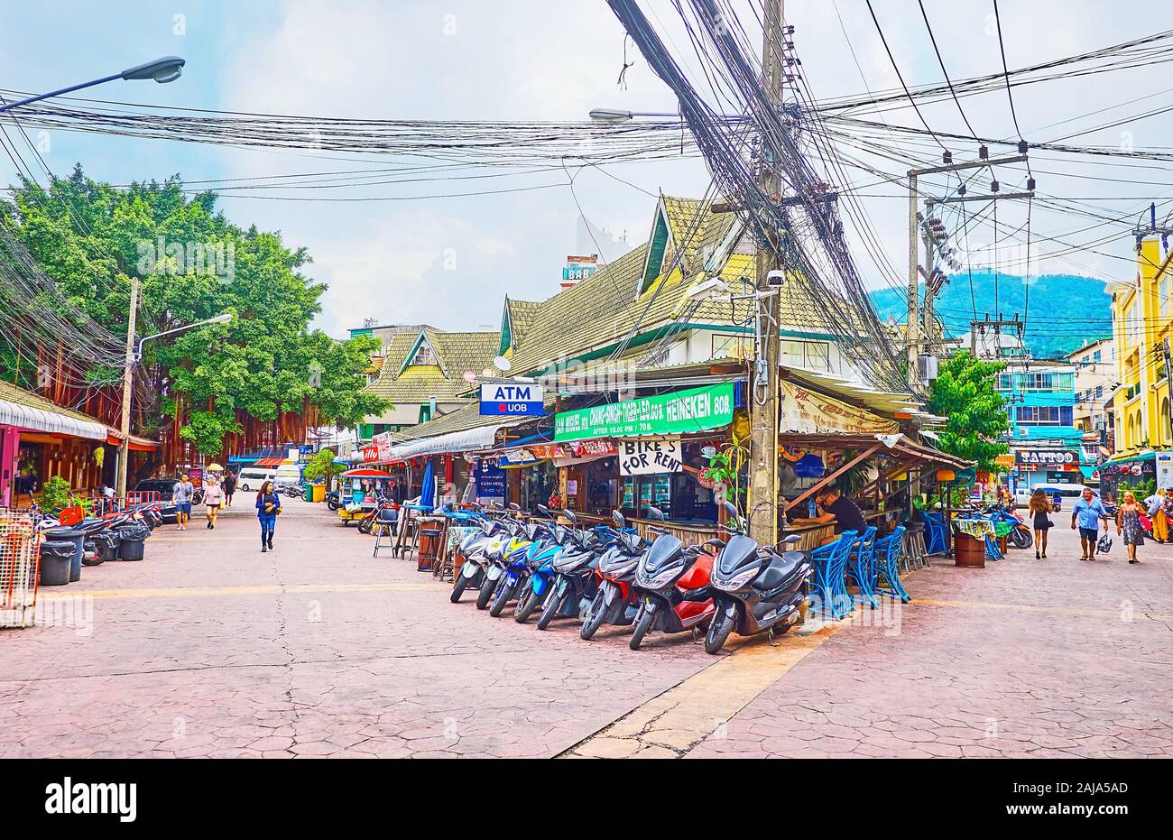 PATONG, Tailandia - 30 Aprile 2019: l'angolo di strada con una vista sulla linea di ristoranti e bar, parcheggio bici e fasci di potenza dangled ca Foto Stock