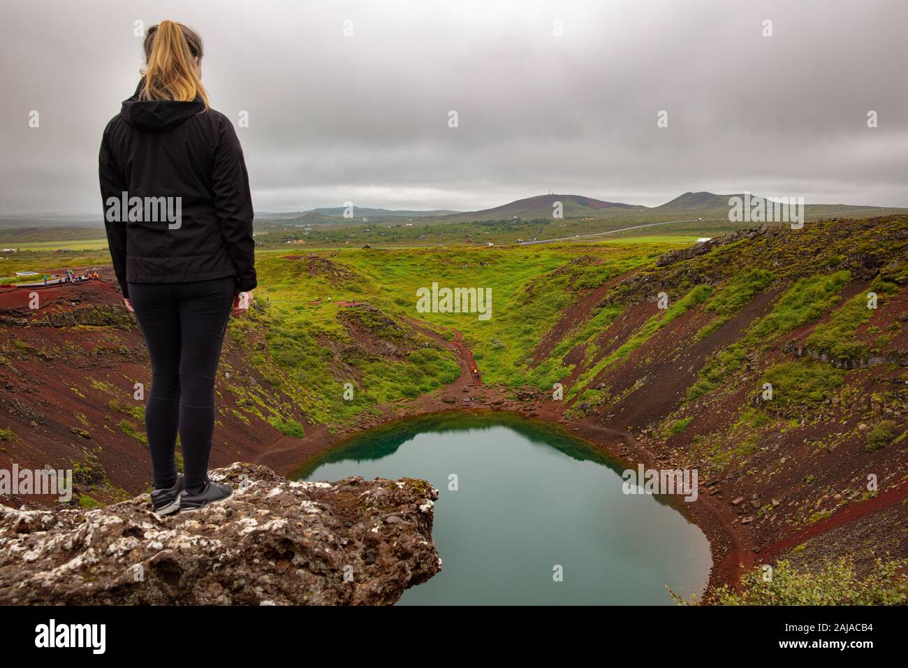 Femmina bionda explorer permanente sulla roccia a guardare Kerid il cratere del lago Foto Stock