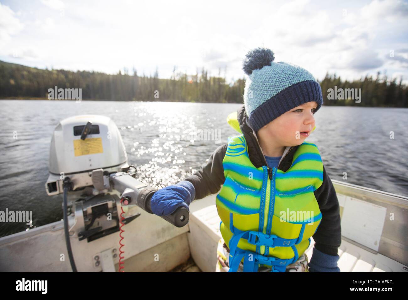 Ragazzo giovane in barca a motore sul lago tranquillo in giornata di sole. Foto Stock