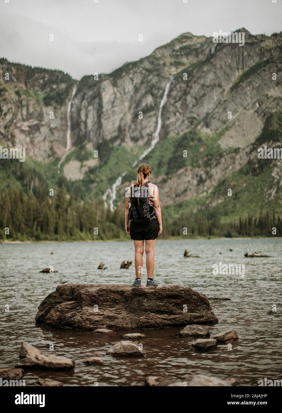 Donna escursionista con zaino si trova sulla roccia a Avalanche Lake, Montana Foto Stock