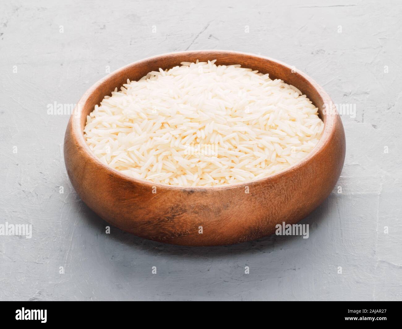 Riso Basmati nella tazza di legno sul cemento grigio e tessuto beige background. Mangiare sano concetto Foto Stock