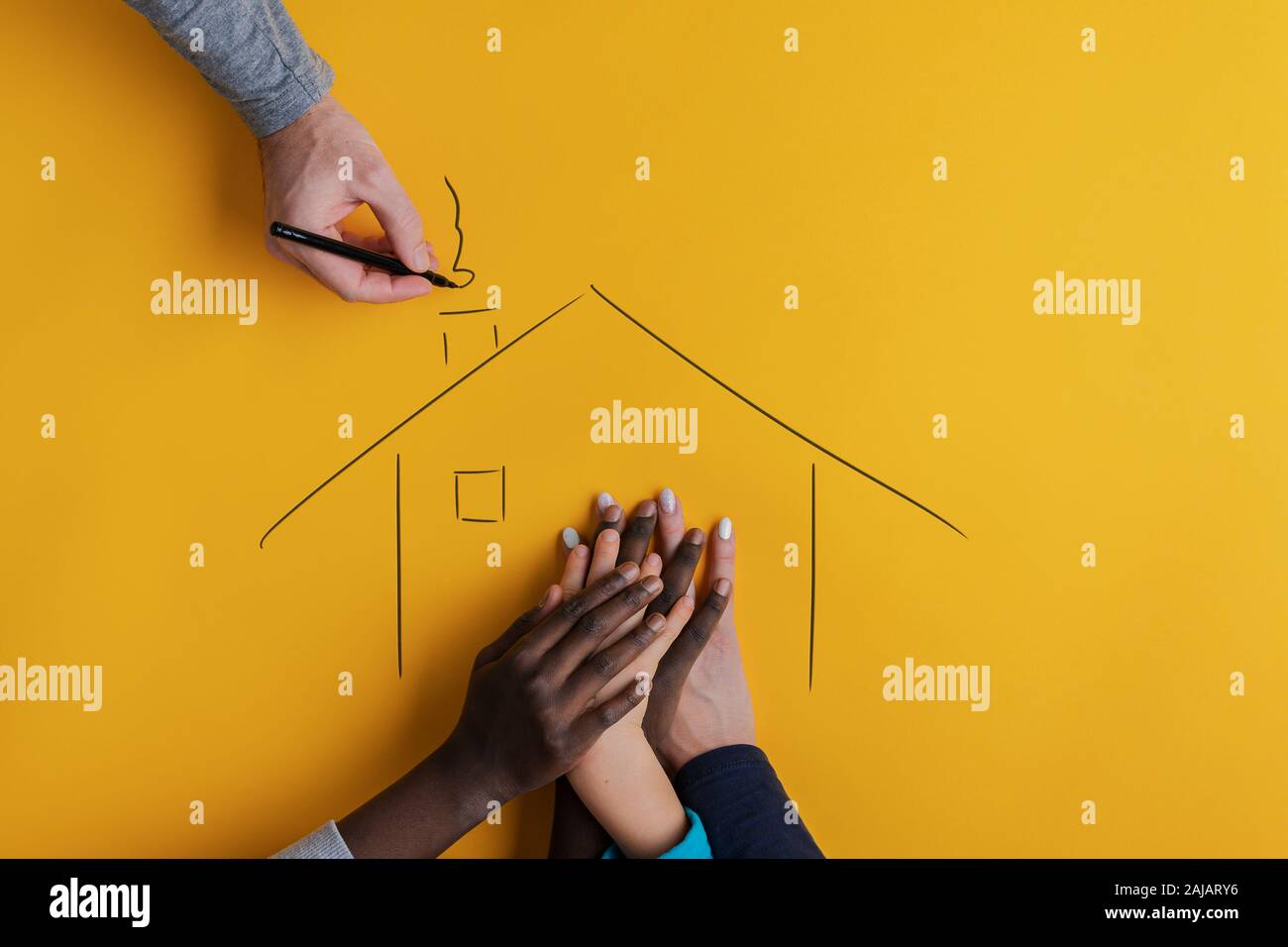 La mano di una madre e tre bambini di soggetti di razza caucasica e ehnicity nero in una casa disegnata a mano dal Padre. Su sfondo giallo. Foto Stock