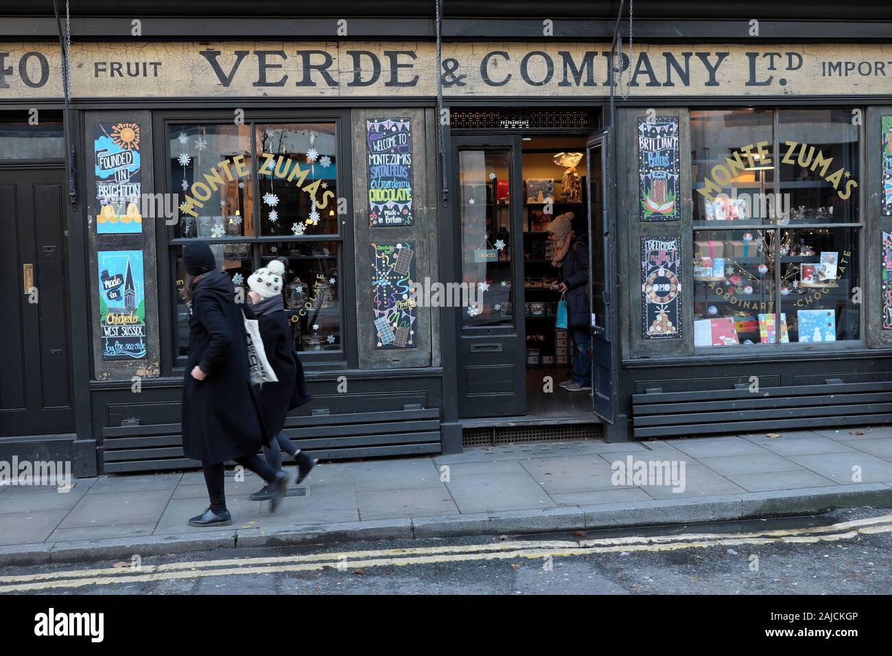 Due persone che camminano passato Natale decorazioni su Verde & Company deli shopfront esterno in Spitalfields East London E1 Inghilterra UK KATHY DEWITT Foto Stock