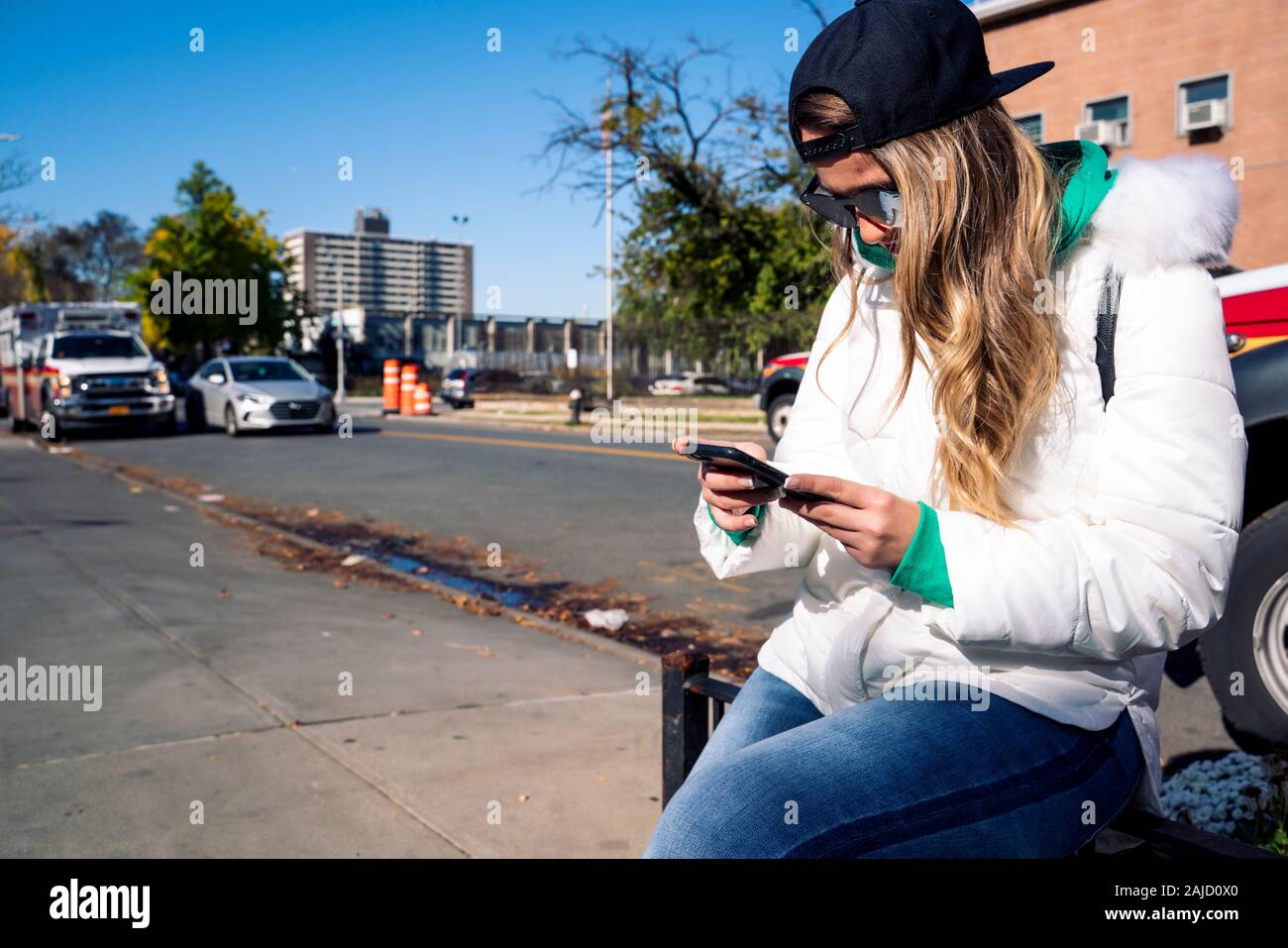 Attraente donna bionda seduta al sole con il suo smartphone Foto Stock