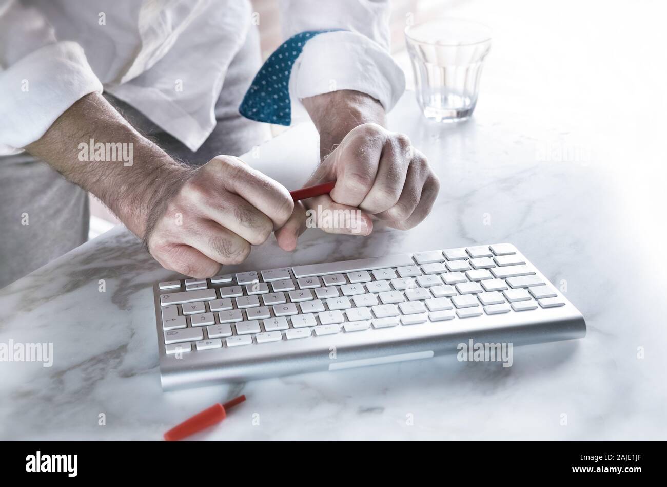 Le mani di un uomo tiene molto stretti la sua penna, dietro la tastiera del computer. Foto Stock