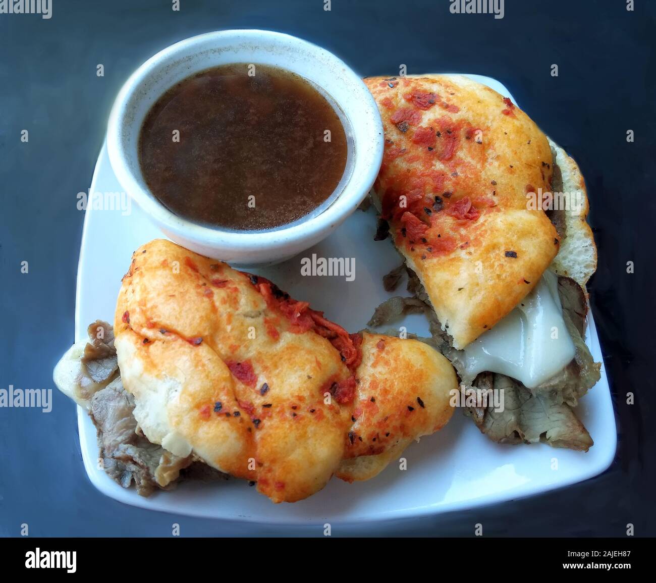 Hot french dip sandwich è servita con fuso mozzarella su una fresca faccocia Pane con pomodori secchi e una tazza di au jus Foto Stock
