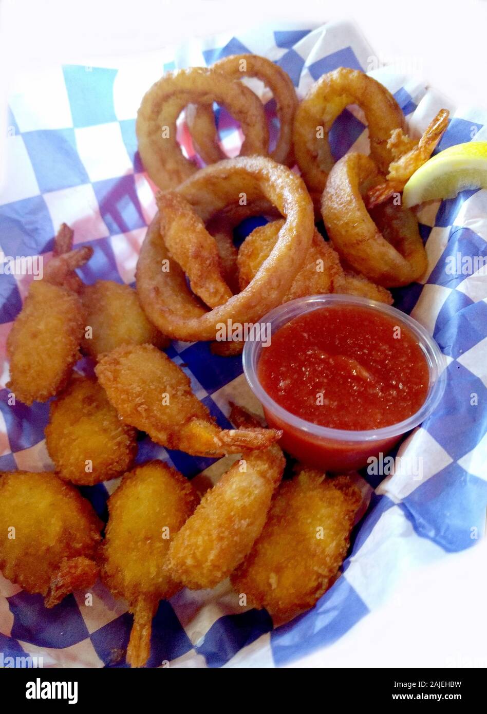 Cesto di croccante frittura di gamberi impanati con anelli di cipolla e un rosso salsa cocktail Foto Stock