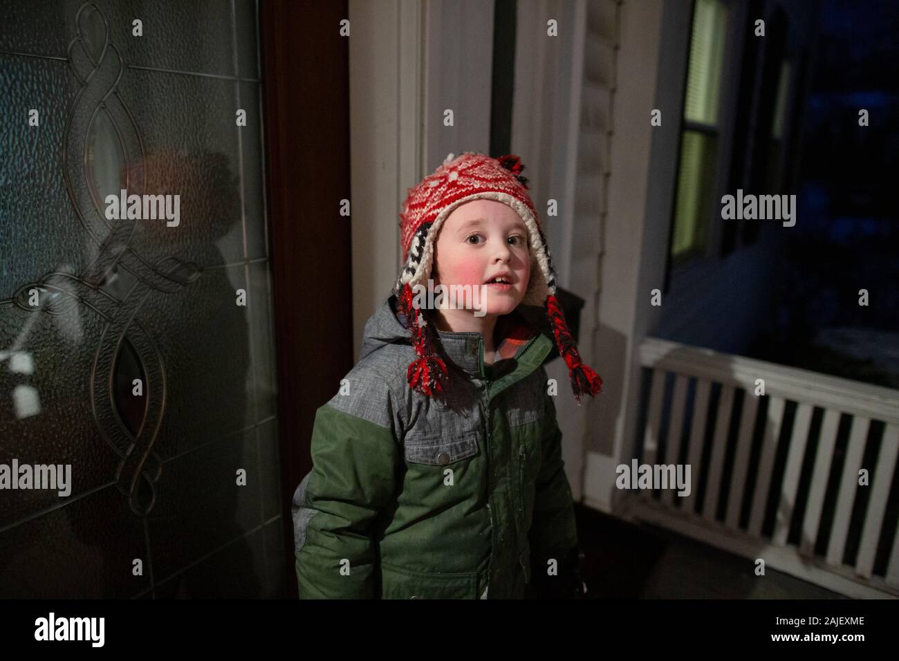 Il ragazzo di età elementare indossa un equipaggiamento per il tempo freddo in piedi di notte sul portico Foto Stock