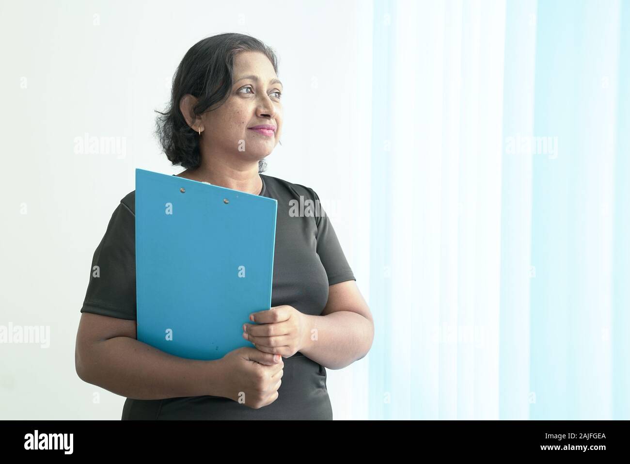 Smart e bellissimo Indian corporate donna con un file di blu in piedi dalle finestre degli uffici. Copia dello spazio. Foto Stock