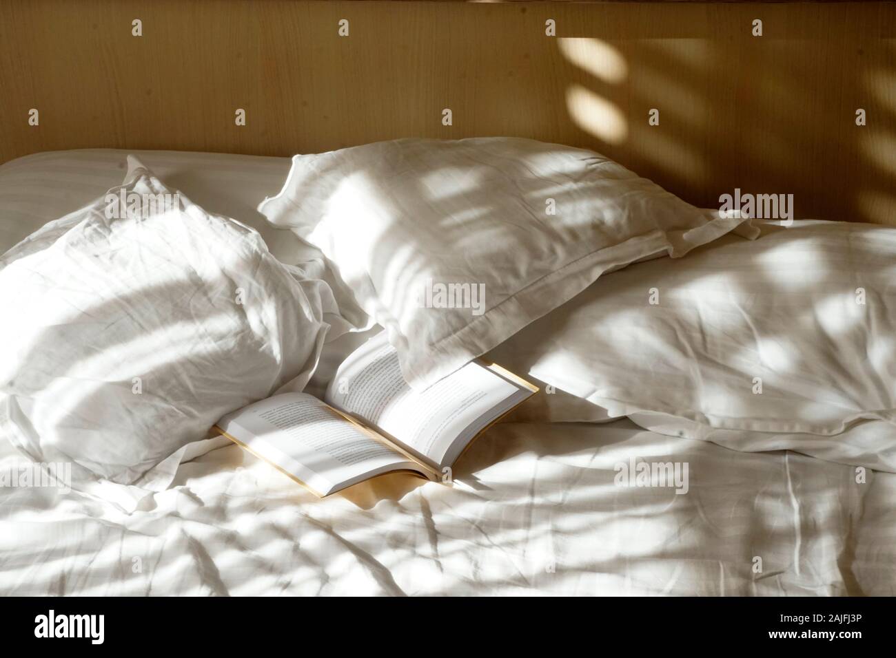Camera da letto in scena con la biancheria bagnata nella luce del mattino. Bella luce sul cuscino e fogli di un letto vuoto e un libro aperto. Foto Stock