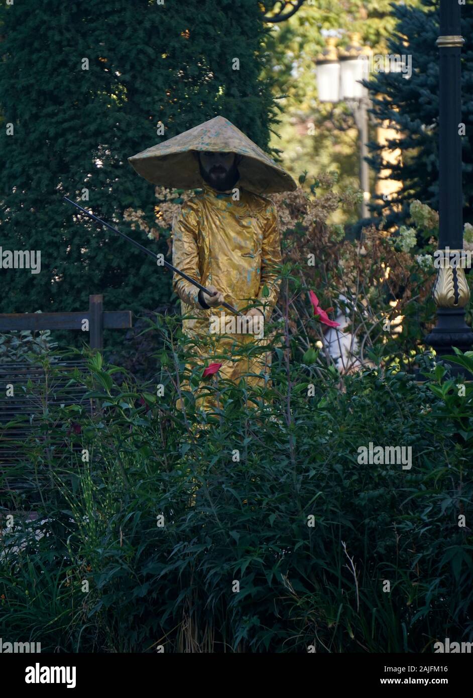 Timisoara, Romania- 09.06.2019 statua vivente di un pescatore cinese. L'uomo vestito di golden cinese tradizionale abbigliamento indossando un asiatico cappello conico po Foto Stock