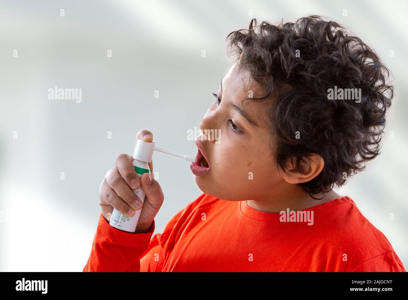 Ragazzo schizza nella sua bocca con uno spray da il dolore nella sua gola. Foto Stock