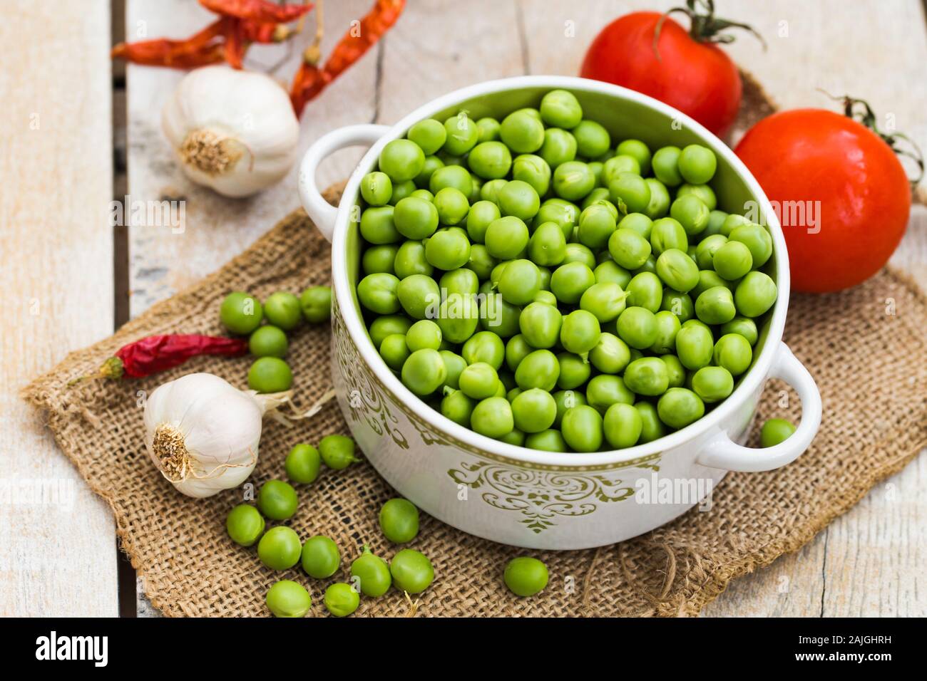 Piselli verdi freschi in una ciotola, pomodori, aglio e pepe rosso, sul tavolo Foto Stock