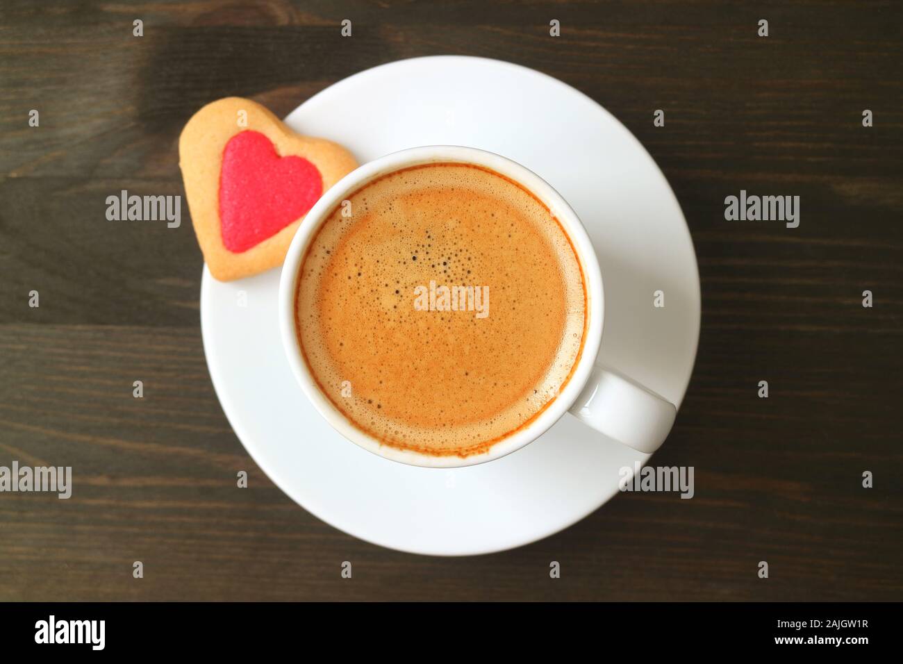 Vista dall'alto di una tazza di caffè con un cuore cookie sagomato in legno marrone scuro e tabella Foto Stock