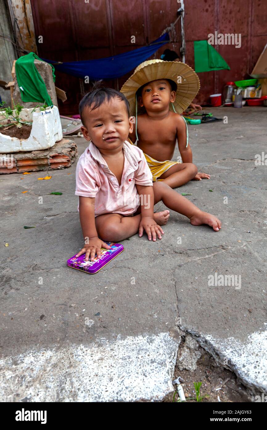 Due poveri giovani ragazzi asiatici sono seduti su un marciapiede davanti a loro scavenger senza dimora della famiglia rifugio di fortuna in Kampong Cham, Cambogia. Foto Stock
