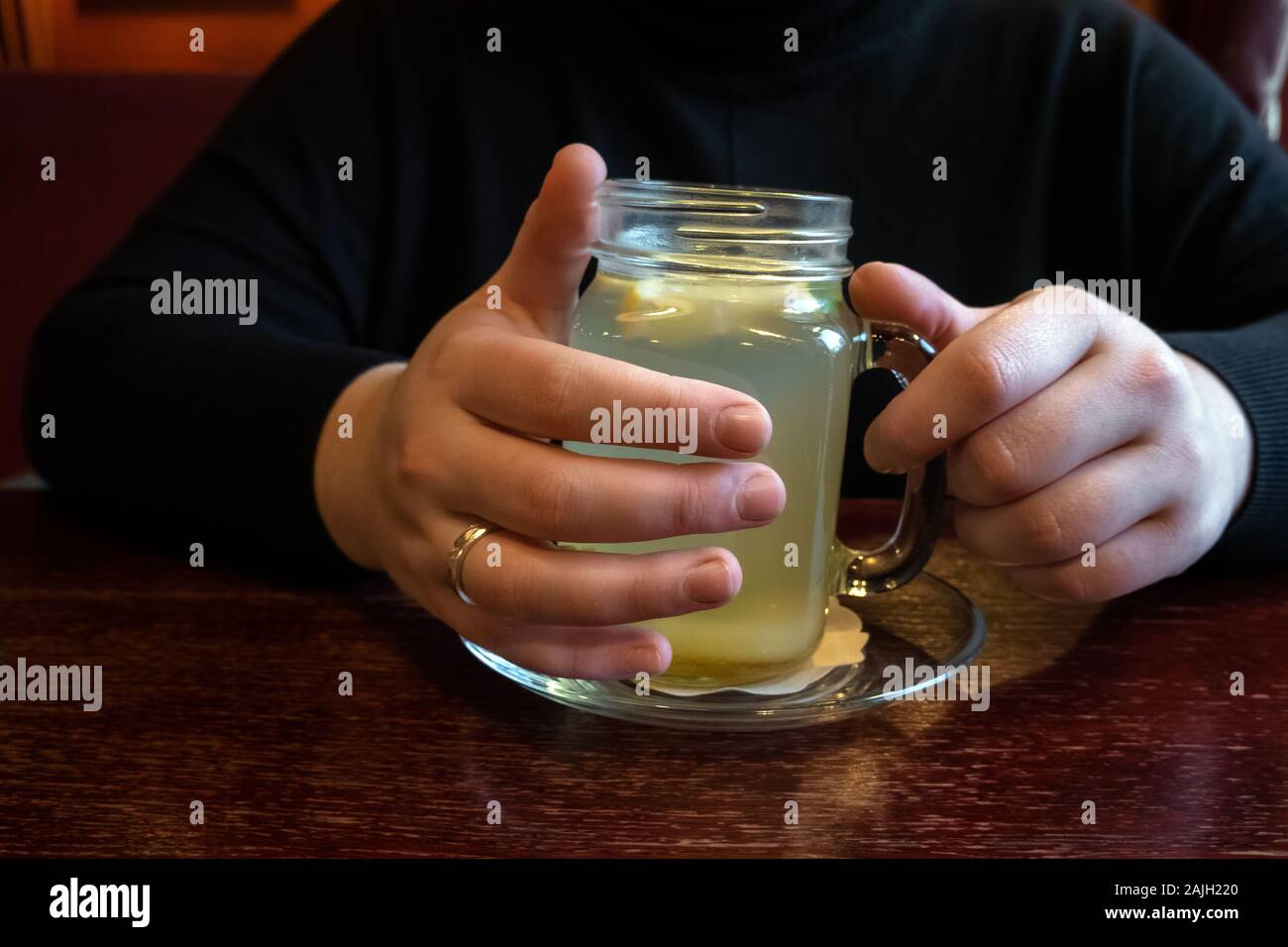 La donna beve caldo e rinfrescante tè allo zenzero con fetta di limone in un ristorante. Mani coppa di ritegno di naturale tè alle erbe su un tavolo di legno, caldo inverno Foto Stock