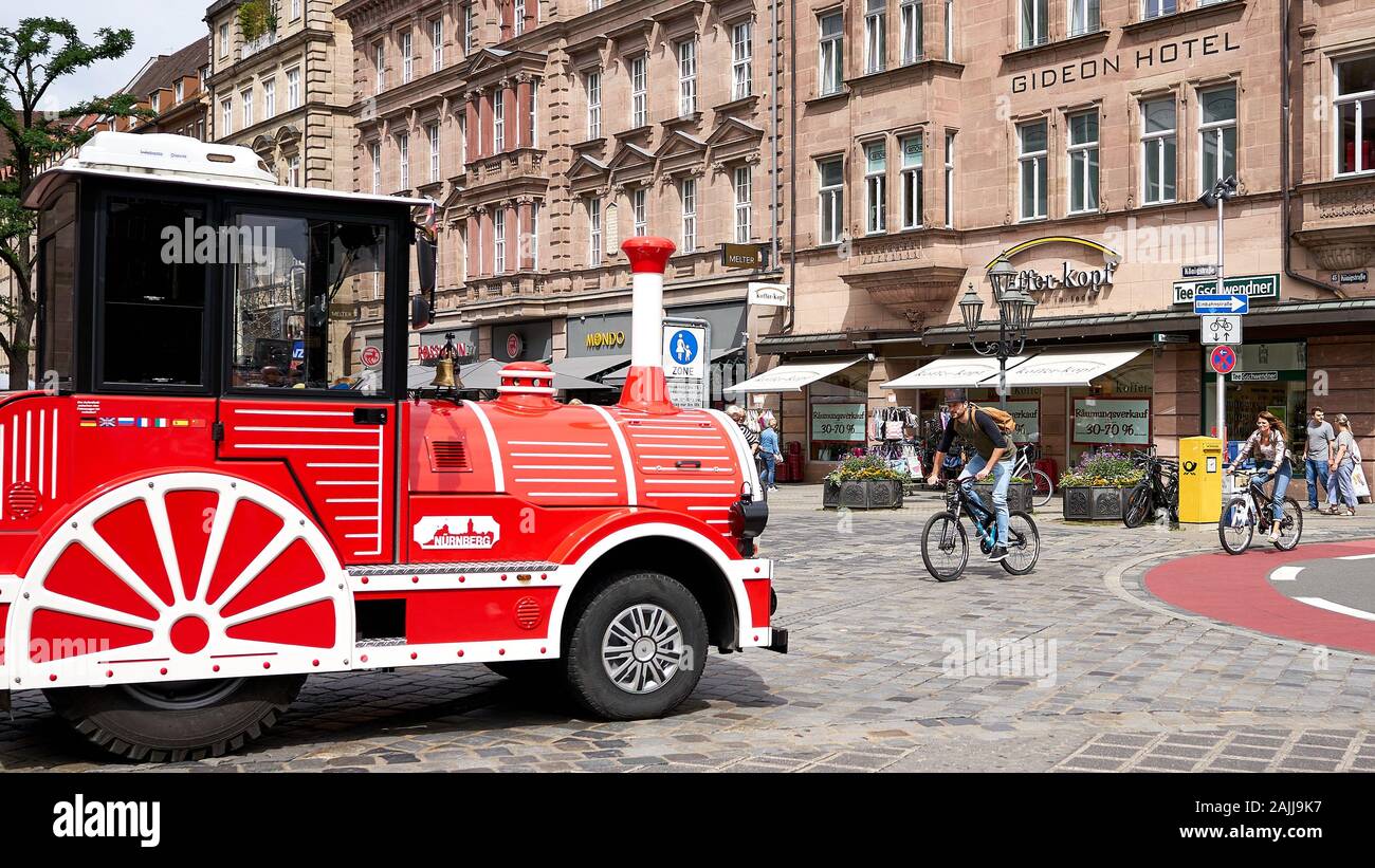 Il motore anteriore di un trolley turistico rosso e di un biciclo maschile sono visti sulla piazza acciottolata nel centro di Norimberga, in Germania Foto Stock