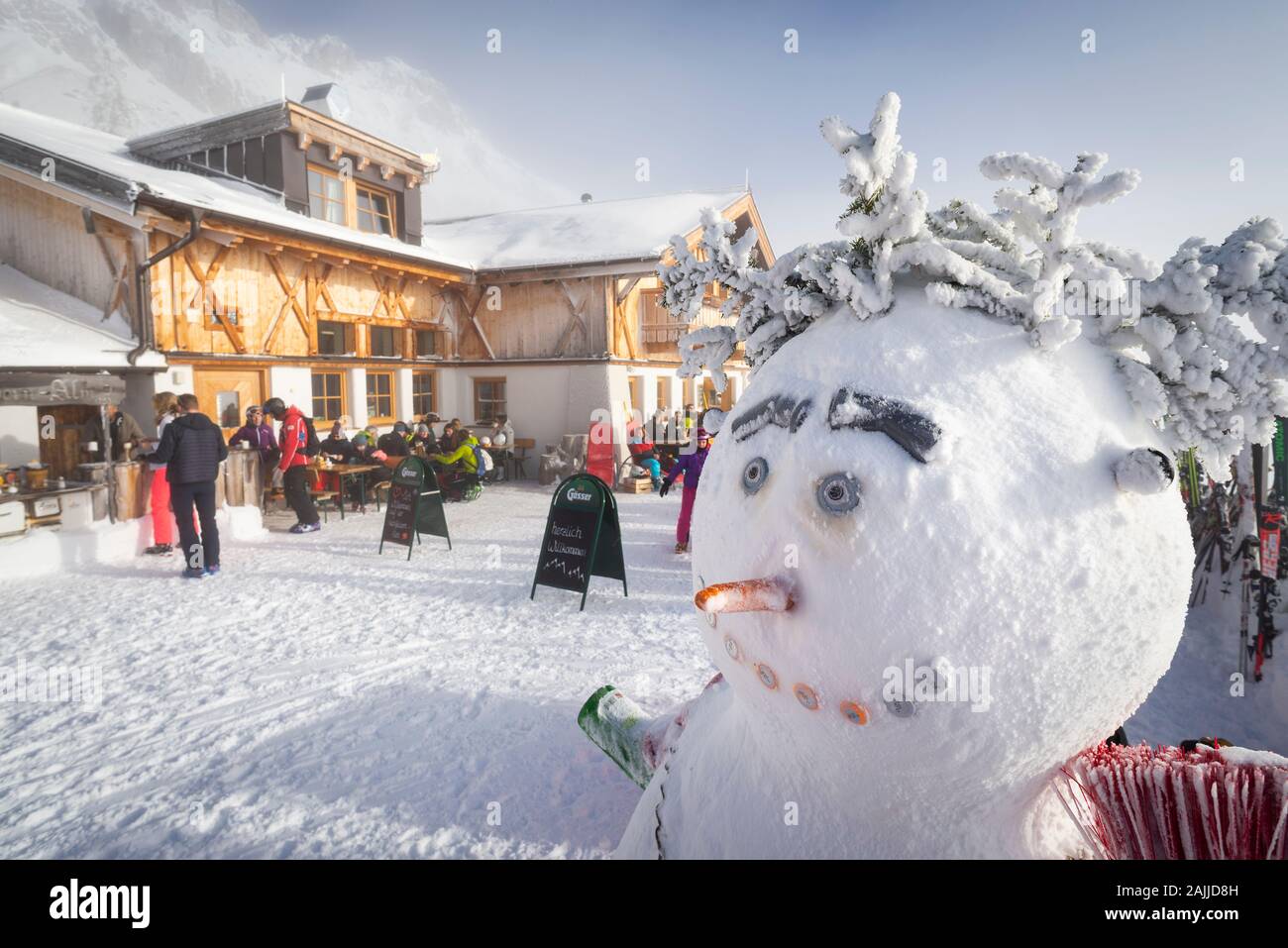 Snowman sulla terrazza soleggiata della baita innevata Hochfeldernalm, ristorante che accoglie gli sciatori nel comprensorio sciistico Ehrwalder Alm, Austria, Tirolo Foto Stock