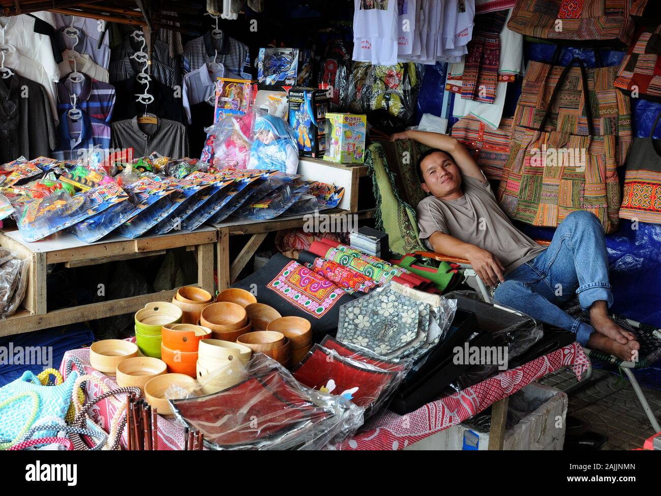 Sorridenti uomo vietnamita in appoggio su una sedia presso il suo negozio di souvenir di Sapa Vietnam Foto Stock