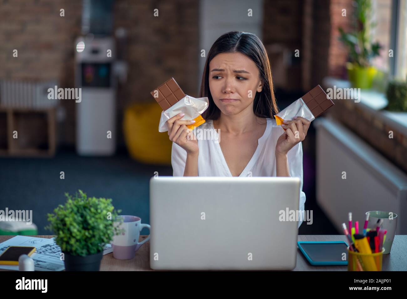 Bella donna triste guardando tenendo due barrette di cioccolato Foto Stock