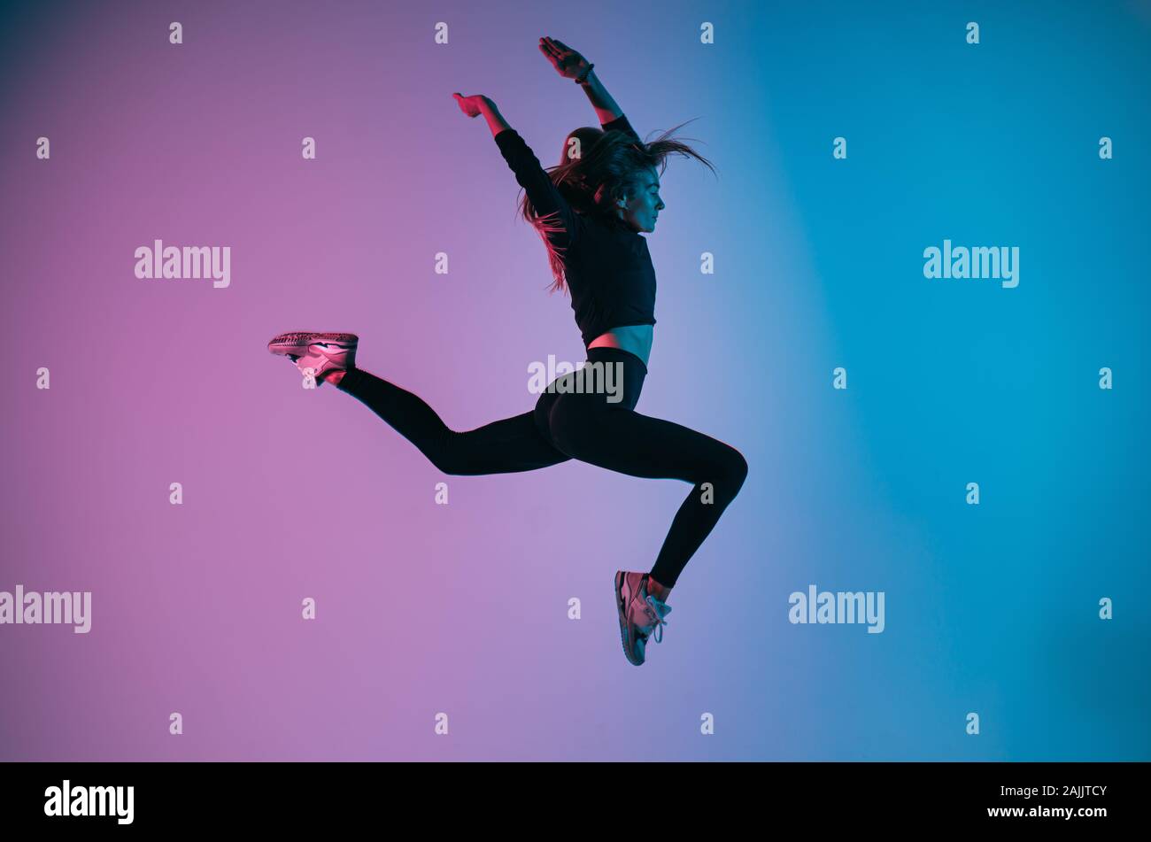Ragazza sportiva nel salto carismatico momento contro alla moda di colore di sfondo. Montare la giovane donna danza jumping. Studio shot Foto Stock