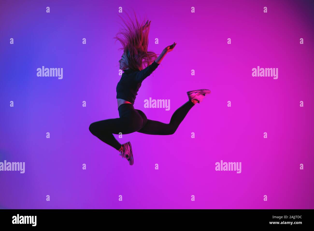 Sportivo da donna carismatica jumping contro colorati di colori alla moda. Atletica Giovane ragazza nel momento di salto in studio Foto Stock