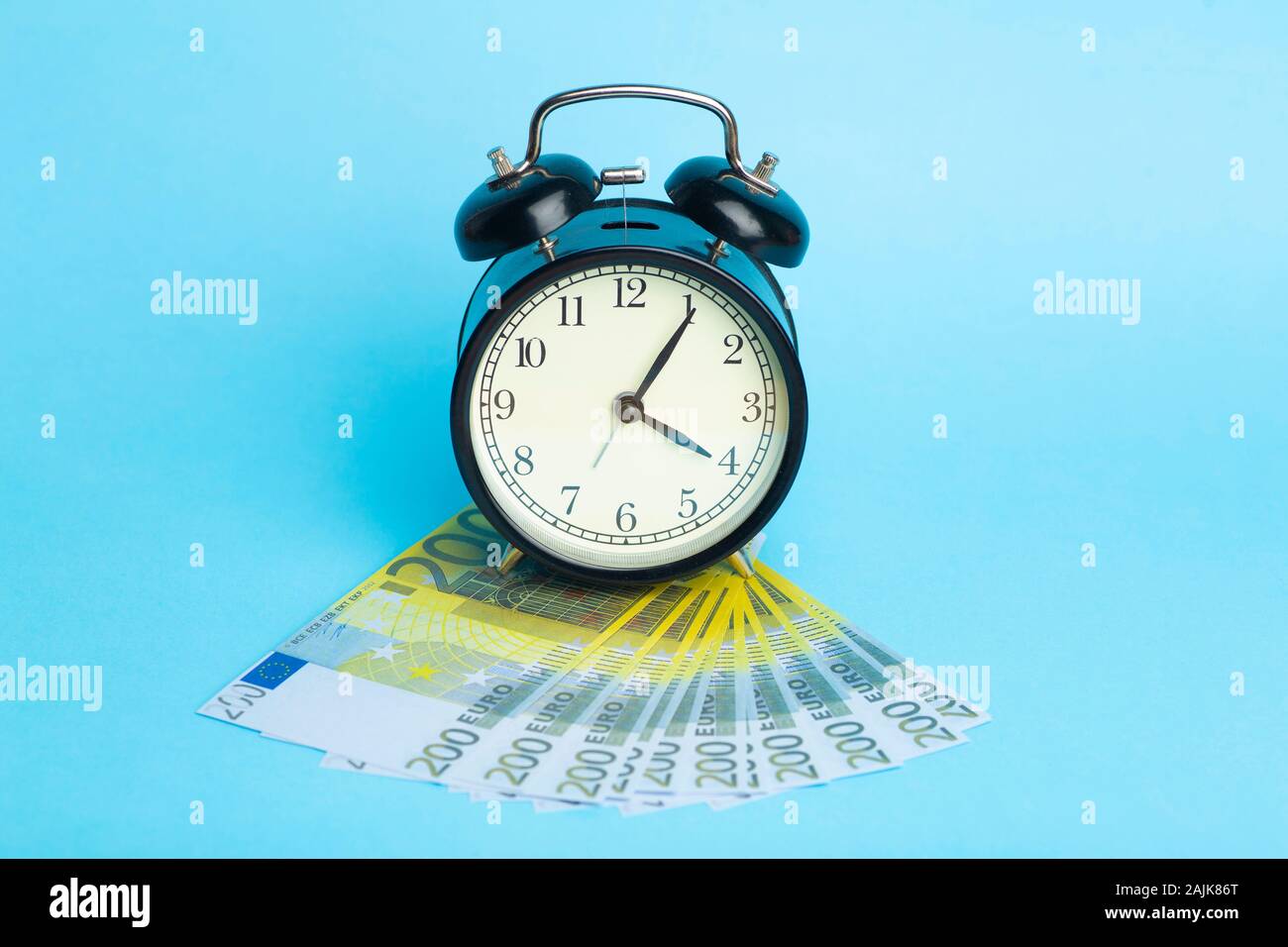 Il tempo e il concetto di denaro. Il contante in euro e sveglia su uno sfondo blu. Foto Stock