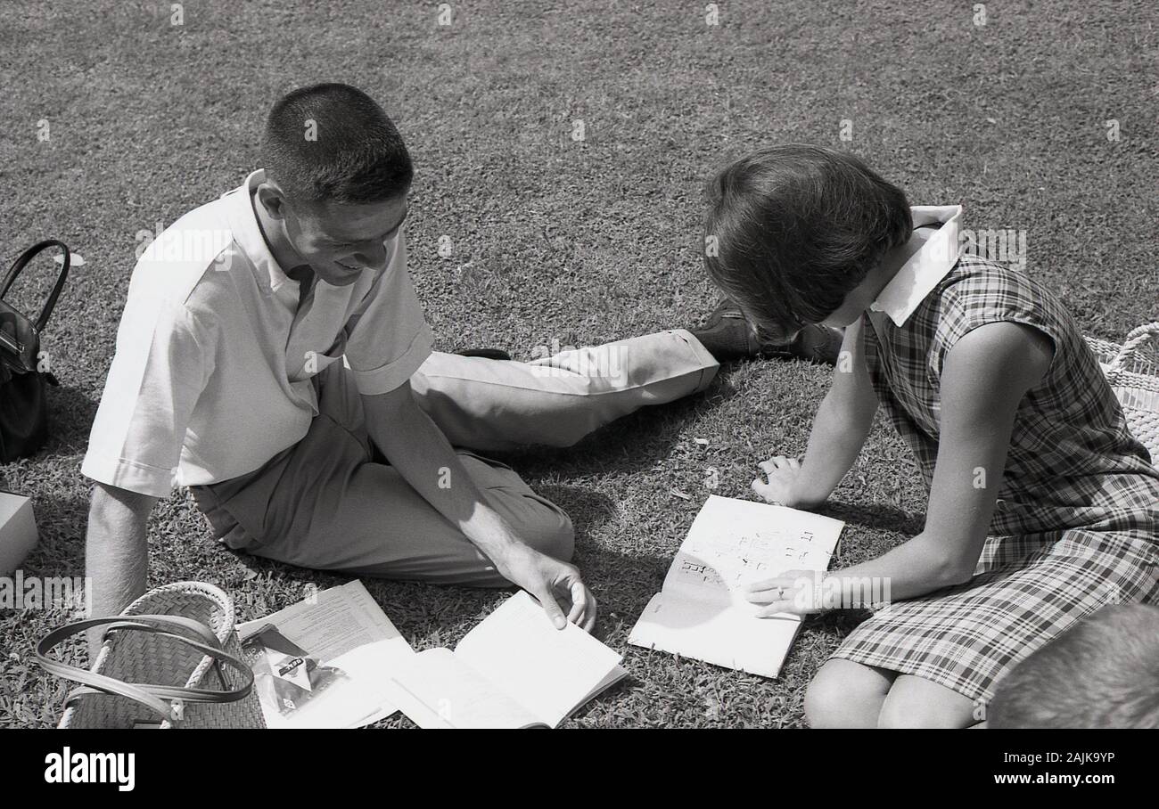 1964, storico, universitari iscritti al "settimana", due studenti di un college americano seduto sull'erba presso il campus guardando alla loro guida Università, California, Stati Uniti d'America. Foto Stock