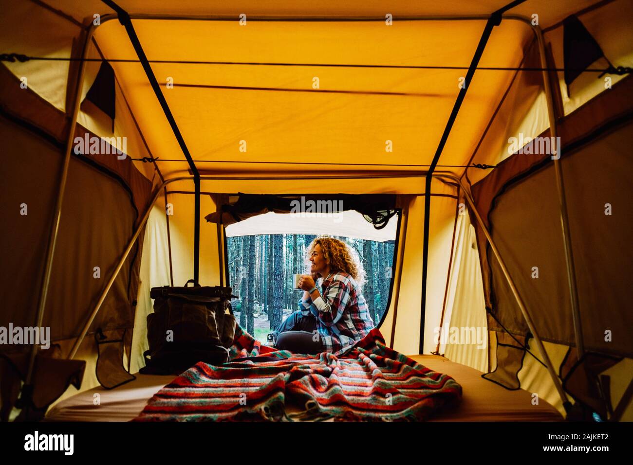 Felice lonely adulto donna caucasica sedersi al di fuori di una tenda gustando una tazza di tè e la selvaggia natura outdoor intorno - alternativa gratuita camping "vacatio Foto Stock