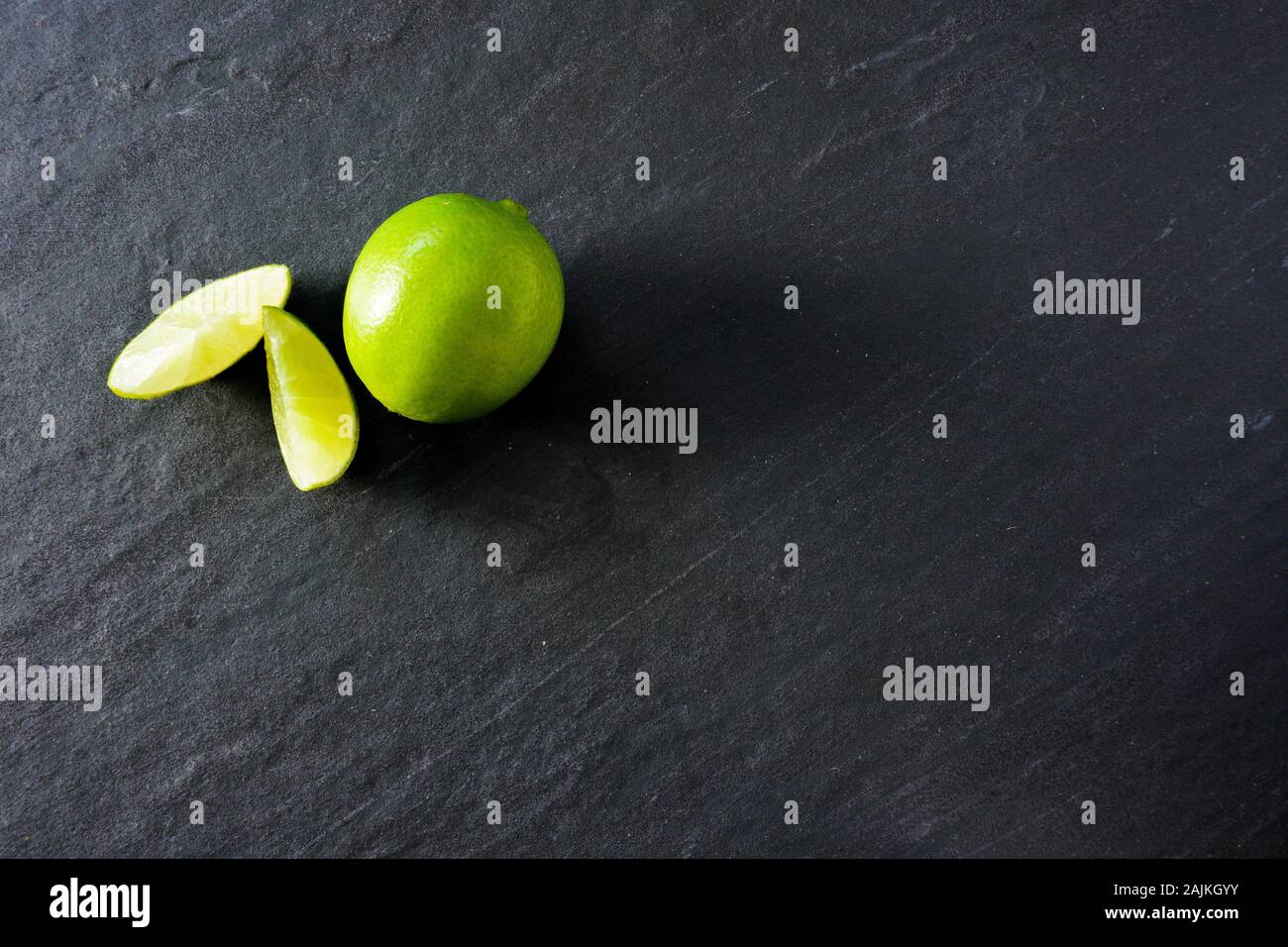 Spicchi di lime accanto a un intero calce pronto a rendere il cocktail di un nero ardesia sfondo; spazio copia a destra Foto Stock