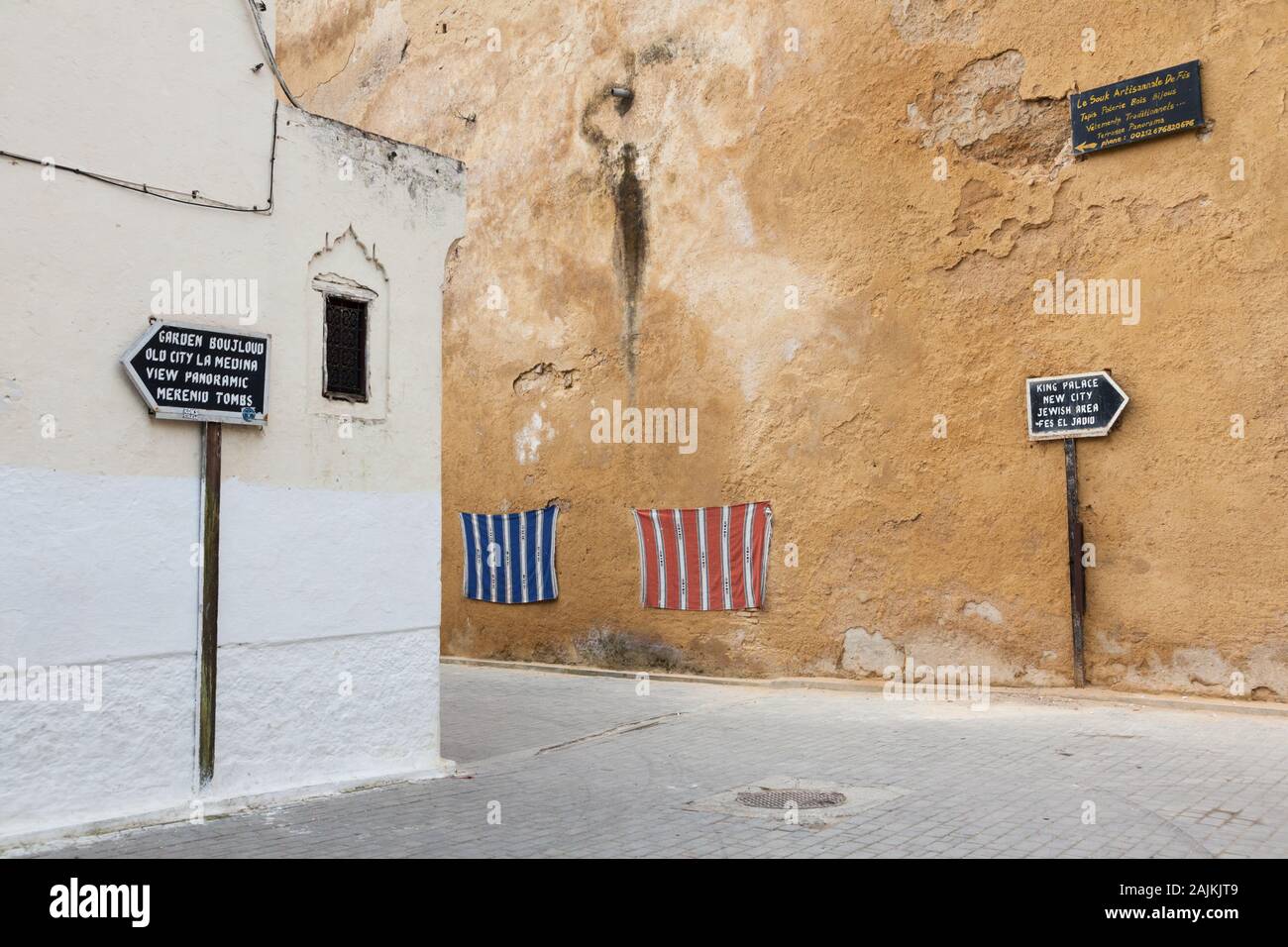 Scenario di Fes (fez) in Marocco con la segnaletica che mostra il modo per le popolari attrazioni turistiche e alcuni tessuti interessanti sulla parete Foto Stock
