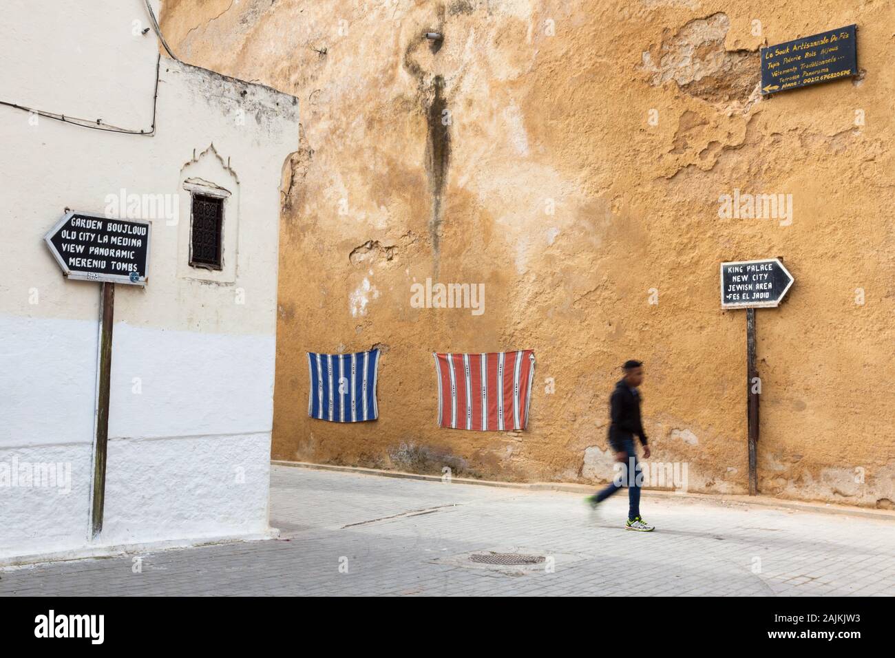 Una silhouette di mosse di pedone, segnaletica mostra modo da popolari attrazioni turistiche e tessuti a righe appesi al muro, Fes (fez), Marocco Foto Stock
