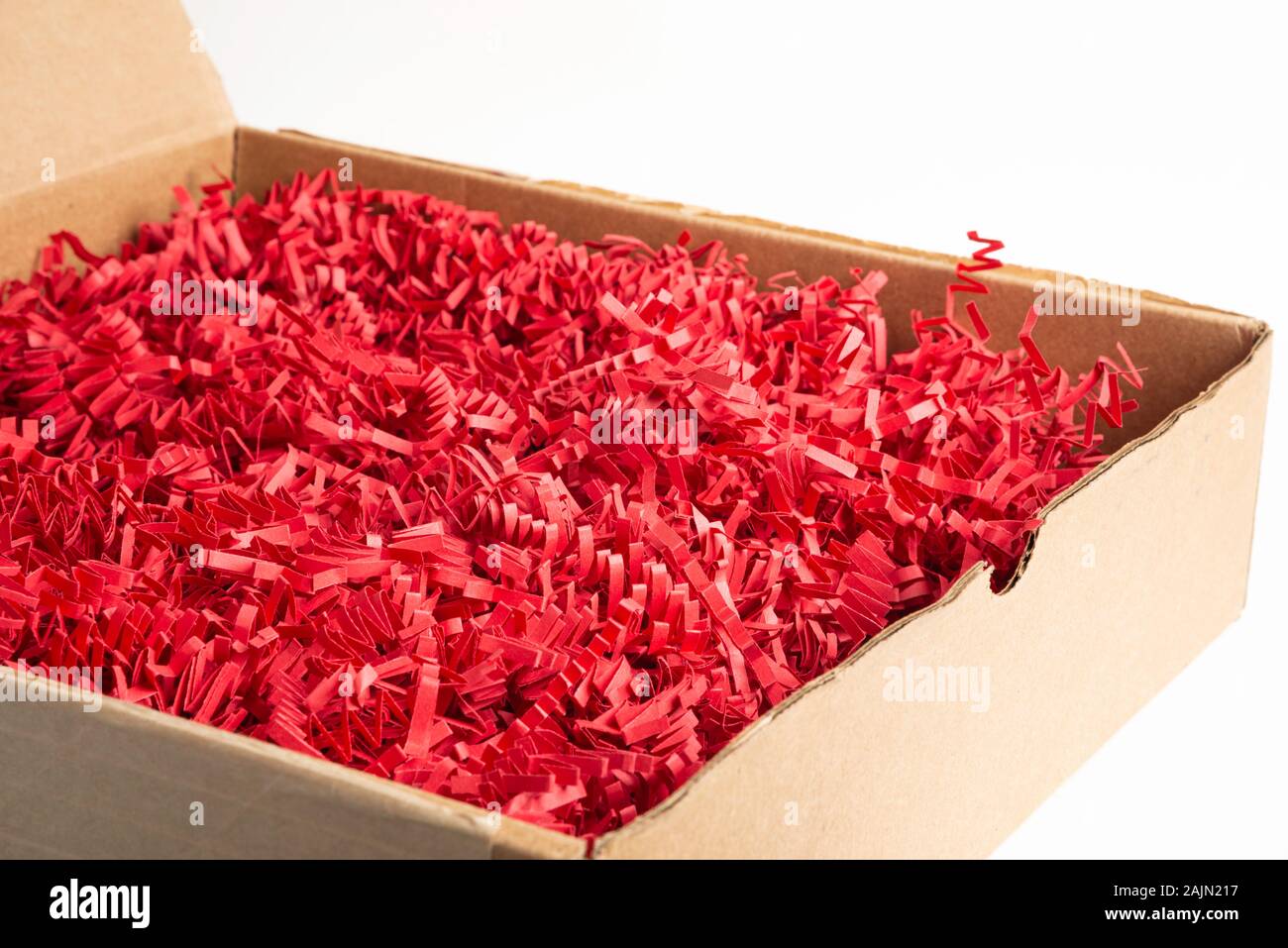 Un marrone confezione di cartone scatola riempita con taglio e aggraffata red strisce di carta impostato su sfondo bianco. Foto Stock