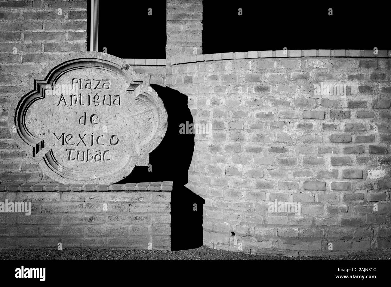 Off centrato vista di un tradizionale canto pietra intagliata per firmare il Plaza Antigua de Mexico in luce cruda contro un vecchio adobe un muro di mattoni in Tubac, AZ Foto Stock