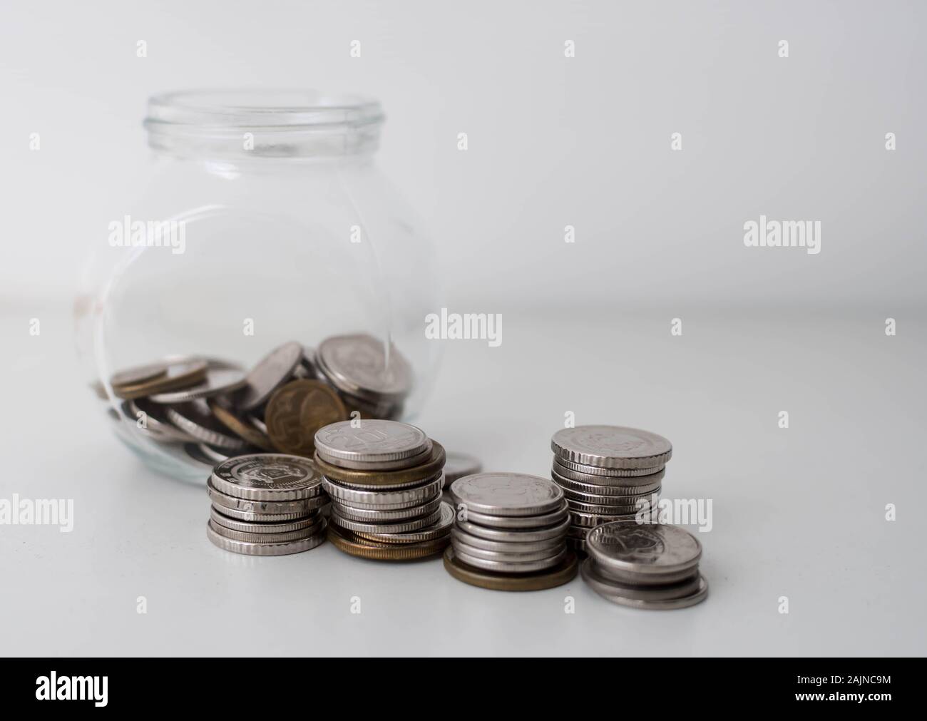 Pila di monete in una bottiglia di vetro su sfondo bianco. Di risparmio e di investimento Concetto del piano. Jar, monete, risparmio, investimenti, donazione. Le monete in un vaso Foto Stock