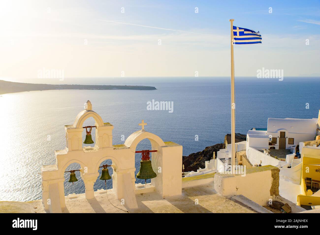 Torre campanaria e la bandiera nazionale della Grecia nella luce del tramonto di Oia - Santorini, Grecia Foto Stock