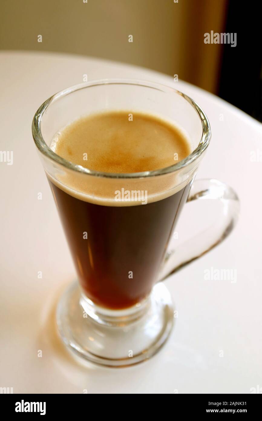 L'immagine verticale a caldo di caffè nero in un vetro trasparente servito su bianco tavola rotonda Foto Stock
