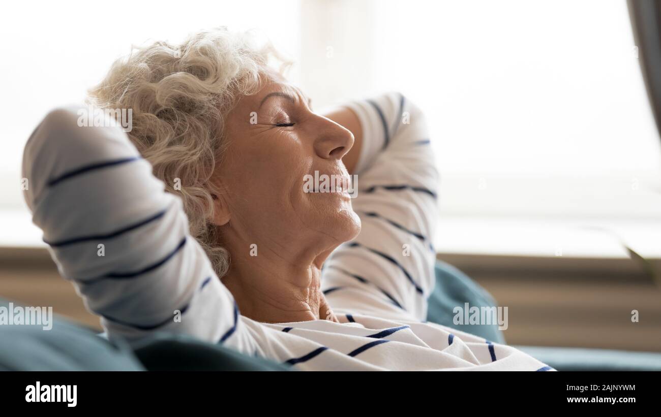 60s donna occhi chiusi mettendo le mani dietro la testa in appoggio in ambienti interni Foto Stock