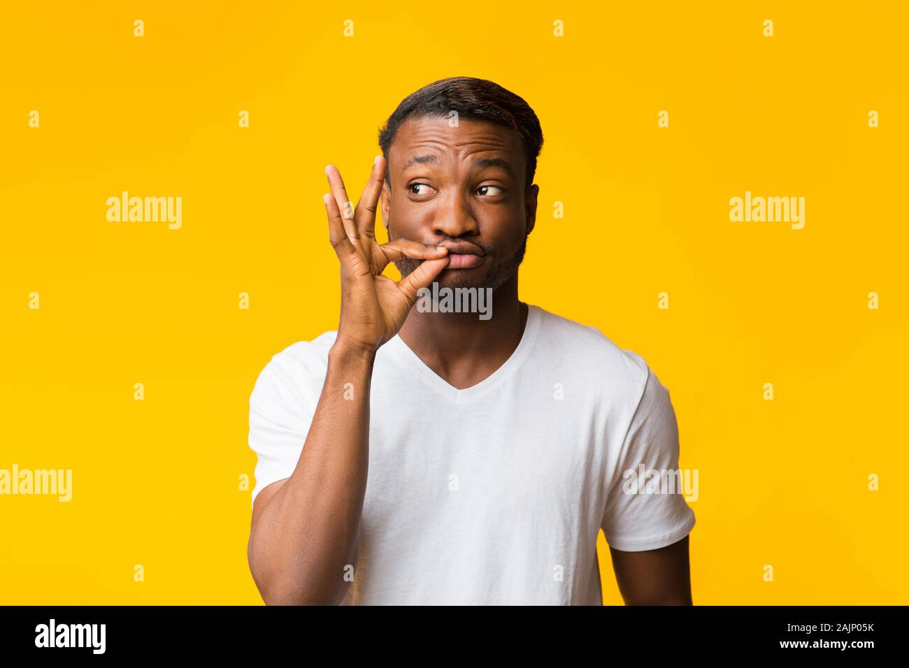 Mantenere segreto. African American Guy gesticolando Zip il tuo labbro in piedi su sfondo giallo. Studio Shot Foto Stock