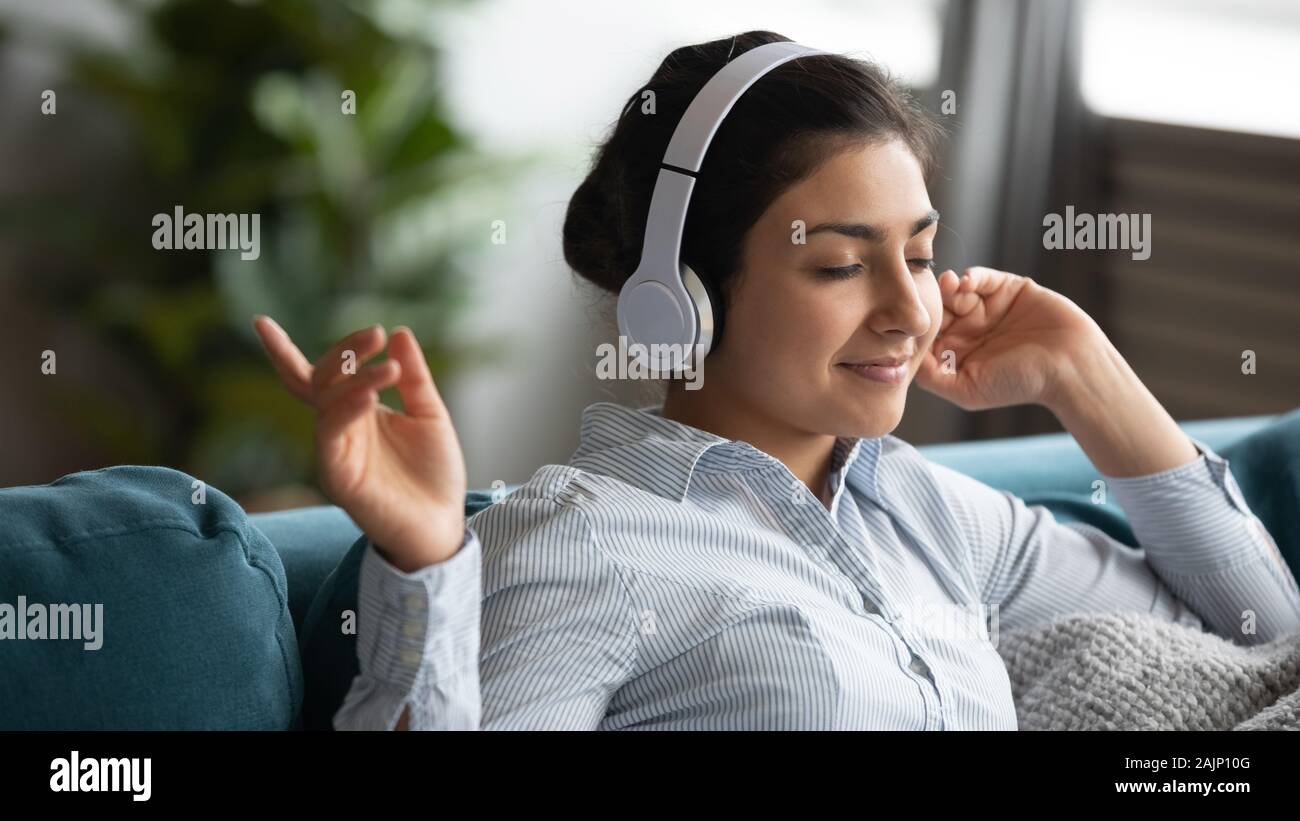 Ragazza indiana indossando le cuffie wireless godendo ascoltando la musica a casa Foto Stock